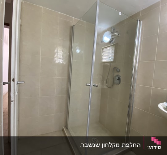 מקלחון פינתי מזכוכית שקופה מותקן בחדר רחצה מרוצף